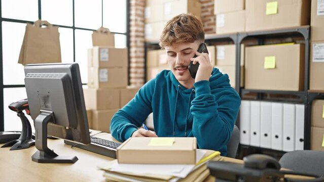 Young hispanic man ecommerce business worker talking on smartphone writing on package at office