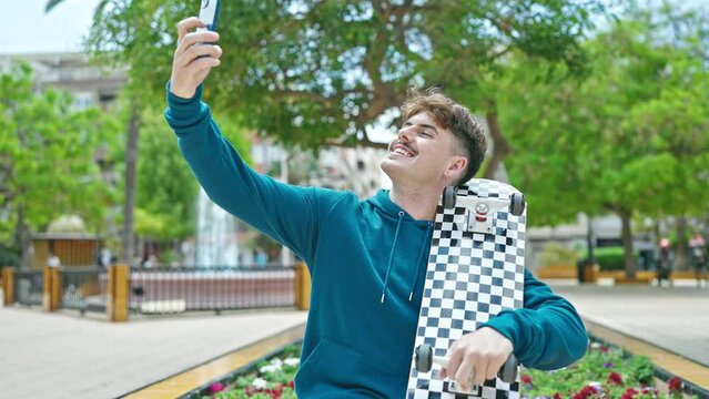 Young hispanic man holding skate make selfie by smartphone at park