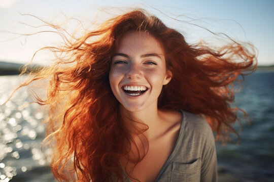 Happy redhead woman with tousled hair by lake