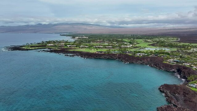 Aerial ocean bay to golf course luxury homes Kona Hawaii 1. Luxury exclusive homes on coast golf course. Economy is tourism based. Volcanic lava rock black sand beach. Water tropical beach recreation.