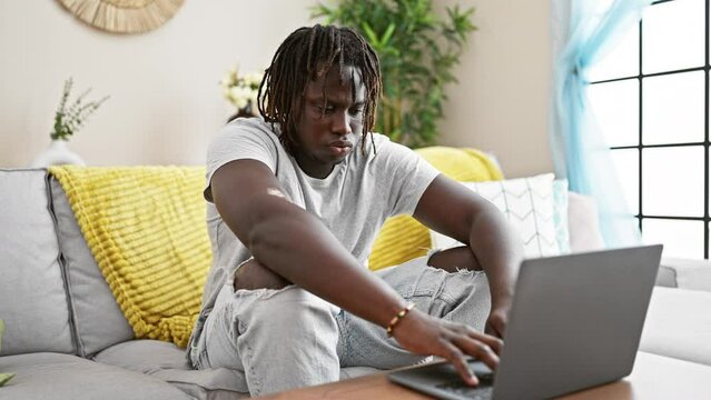 African american man closing laptop lying on sofa covering face with cushion at home