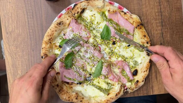 man eats traditional Italian pizza with mortadella, mozzarella cheese, pistachios and pesto.