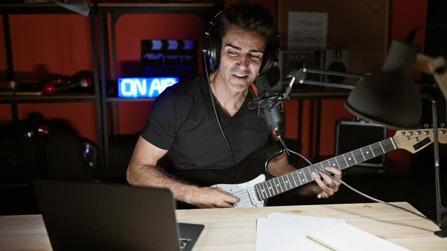 Young hispanic man musician singing song playing electrical guitar at radio studio