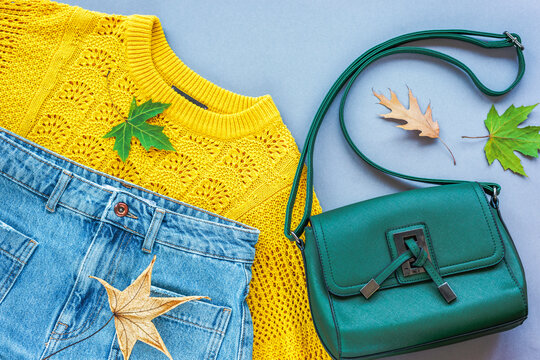 Flat lay of woman's yellow sweater, jeans, green bag and autumn leaves on grey background. Autumn fashion concept. Top view, flat lay - Powered by Adobe