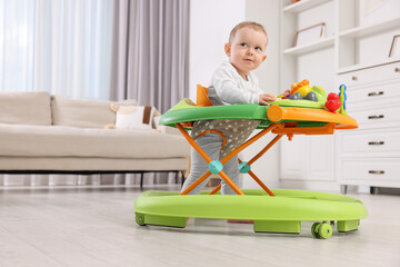 Cute little boy making first steps with baby walker at home