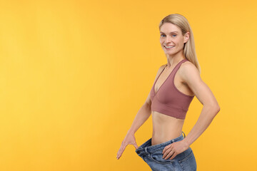 Slim woman wearing big jeans on yellow background, space for text. Weight loss