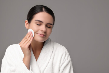 Young woman cleaning her face with cotton pad on grey background. Space for text