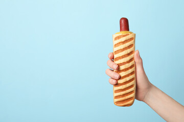 Woman holding delicious french hot dog on light blue background, closeup. Space for text