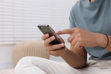Man sending message via smartphone indoors, closeup