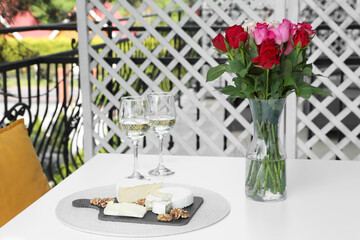 Fototapeta na wymiar Beautiful roses, glasses of wine and snacks on white table at balcony