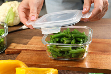 Woman closing container with lid at table, closeup. Food storage