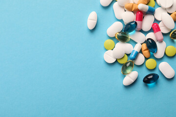Pile of different pills on light blue background, flat lay. Space for text