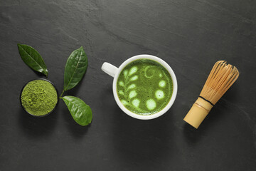 Delicious matcha latte, powder, leaves and whisk on dark textured table, flat lay