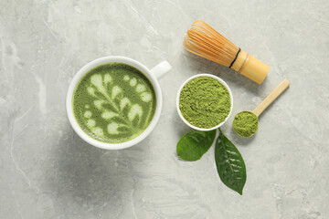 Delicious matcha latte, powder, leaves and whisk on grey textured table, flat lay