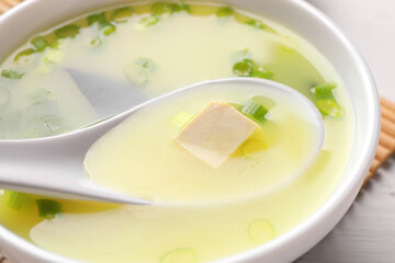 Bowl of delicious miso soup with tofu and spoon on table, closeup