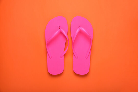 Stylish pink flip flops on orange background, top view