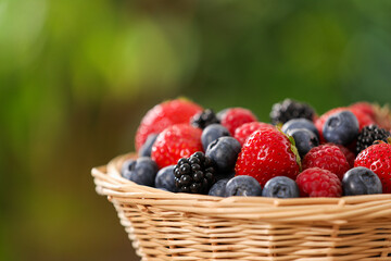 Wicker bowl with different fresh ripe berries outdoors, closeup. Space for text