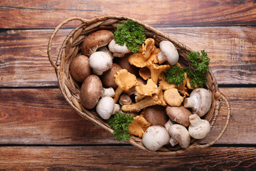 Basket with different mushrooms on wooden table, top view