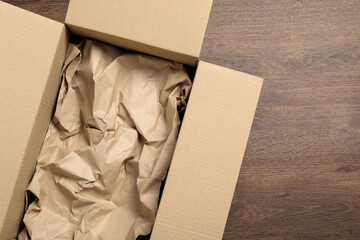 Open cardboard box with crumpled paper on wooden floor, top view and space for text. Packaging goods