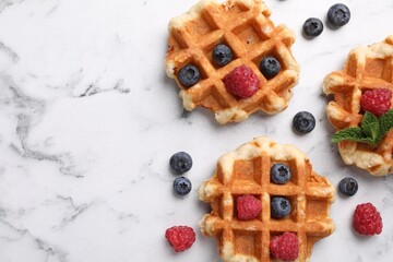 Delicious Belgian waffles with fresh berries and mint on white marble table, flat lay. Space for text