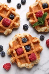 Delicious Belgian waffles with fresh berries and mint on white marble table, flat lay