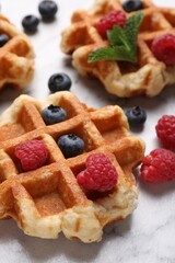 Delicious Belgian waffles with fresh berries and mint on white table, closeup