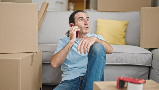 Middle age man speaking on the phone sitting on floor at new home