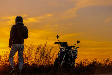silhouette of a biker in a helmet near a motorcycle at sunset.