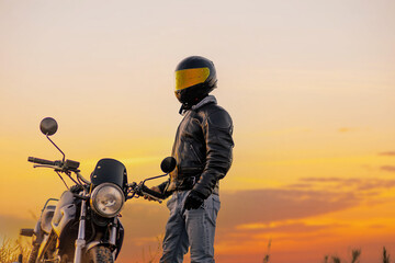 motorcyclist in a helmet and leather jacket at sunset with a classic motorcycle. Moto life concept