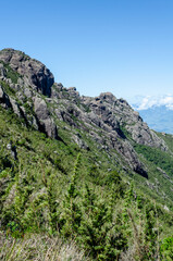 mountainous landscape with a clear blue sky. The mountain is covered in green vegetation and has a rocky cliff face.
