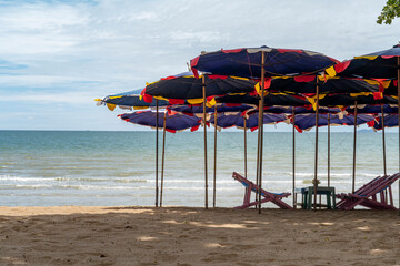 On the seashore there are sun loungers and parasols against the background of a blue sky with clouds. Umbrellas are inserted into the sand of the sandy beach. Small waves roll onto the shore.