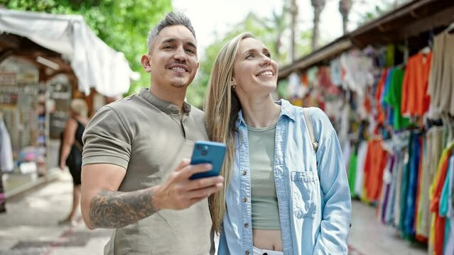 Man and woman couple smiling confident using smartphone at street market