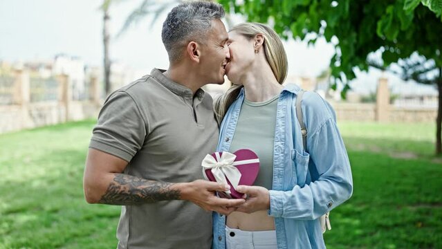 Man and woman couple holding heart package gift kissing at park