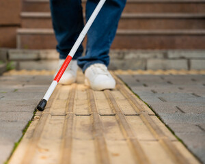 A blind woman walks outdoors using a cane along a tactile yellow tile.