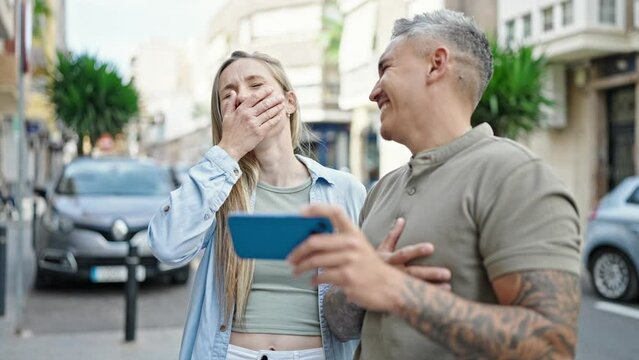Man and woman couple watching video on smartphone laughing a lot at street