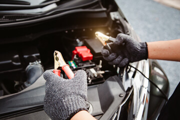 Close-up hand auto mechanic using connect jumper cables on terminal dead battery for jump-start or...