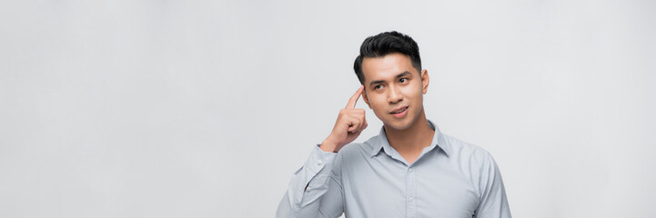 Young man smiling pointing to head with one finger, great idea or thought, good memory
