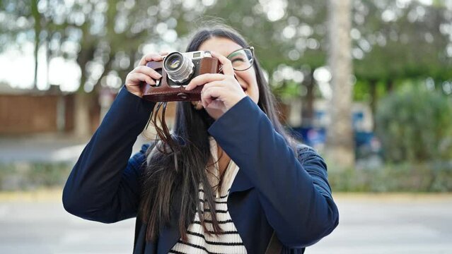 Young hispanic woman tourist wearing backpack taking pictures with camera at street