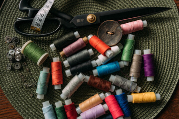 Fototapeta na wymiar multicolored spools of thread, white sewing tape, buttons, black scissors, buttons are scattered on the table. Preparation for sewing. Tailor's table. Creative mess