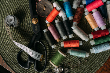 multicolored spools of thread, white sewing tape, buttons, black scissors, buttons are scattered on the table. Preparation for sewing. Tailor's table. Creative mess