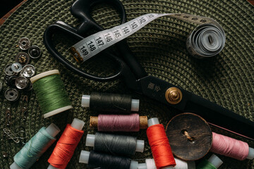 multicolored spools of thread, white sewing tape, buttons, black scissors, buttons are scattered on...