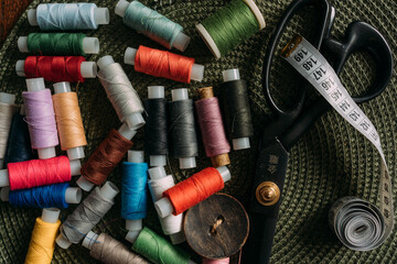 multicolored spools of thread, white sewing tape, buttons, black scissors are scattered on the...