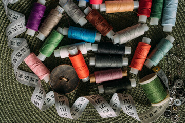 Fototapeta na wymiar multicolored spools of thread, white sewing tape, buttons are scattered on the table. Preparation for sewing. Tailor's table. Creative mess