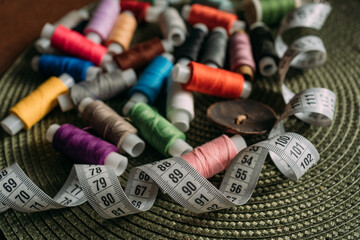 multicolored spools of cotton thread, white sewing tape, buttons are scattered on the table....