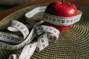 a white centimeter-long sewing tape is wrapped around an red apple, an analogy with the waist. The...