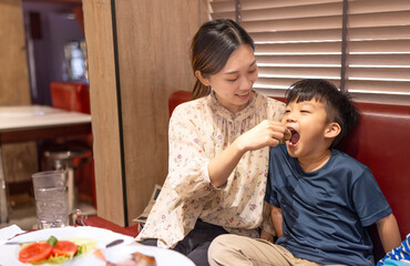  Happy mother feeds her son in restaurant