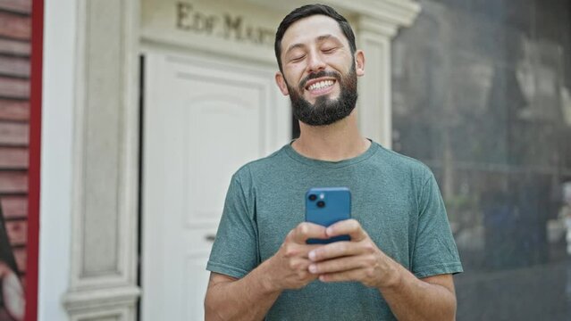 Young hispanic man using smartphone smiling at street