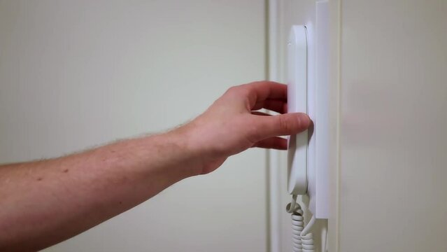 Close up of a hand picking up intercom handset and opening the door
