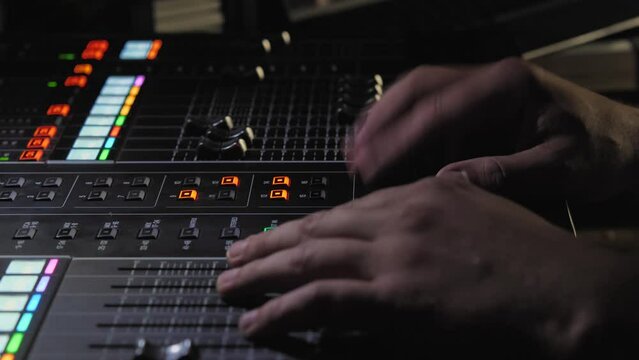 A sound engineer working behind a digital sound mixer. Side view from the top. Dark studio or sound engineer's room at a concert. Men's hands controlling the sound at an event
