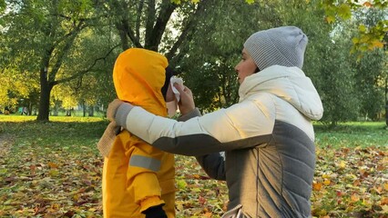 mother squeezing her child running nose in the autumn park - Powered by Adobe